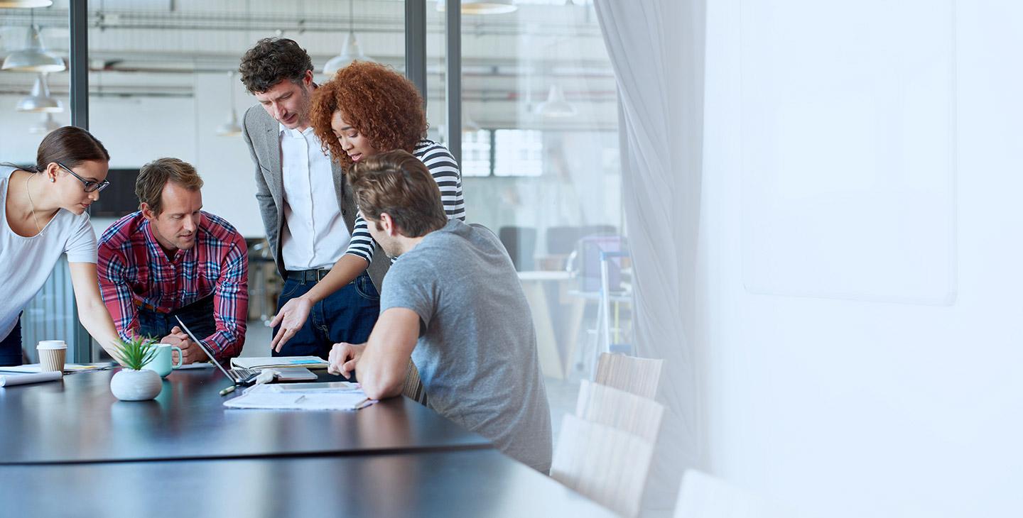 Five co-workers discussing custom antenna design at a large conference room desk